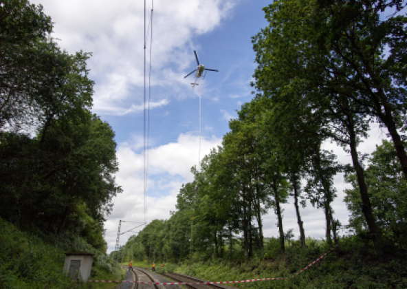Helikopter mit einer meterlange Säge über Bahngleisen